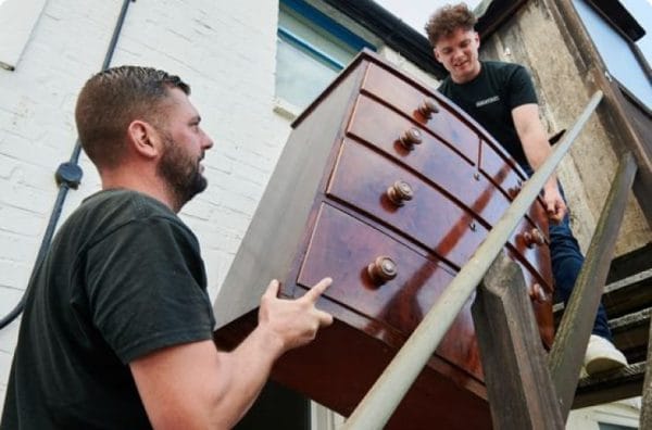 Two men carrying old furniture as part of a flat clearance