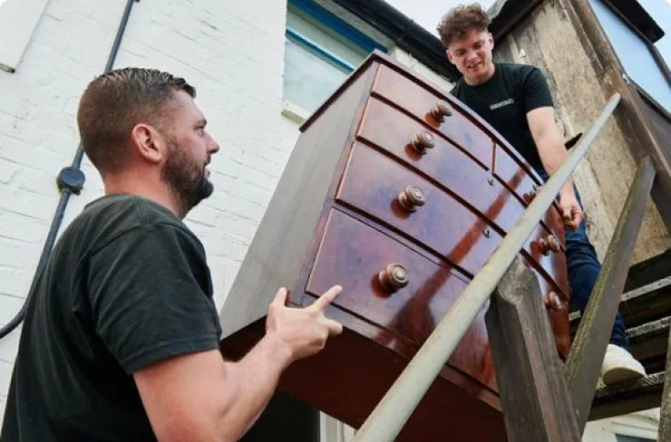 Two men carrying old furniture as part of a flat clearance